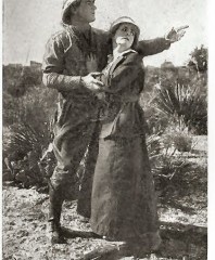 black and white image of man in pith helmet gesturing to distance while woman clings to him