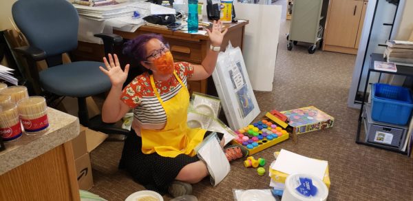 A library worker sits on the floor, assembling bags with summer reading craft materials.